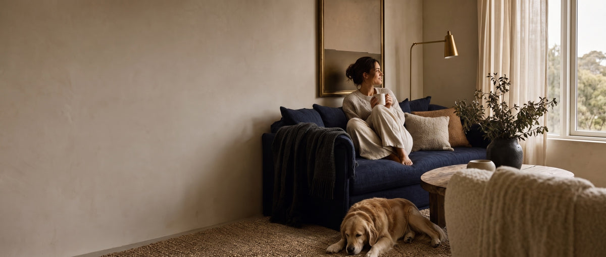 A woman with a mug on a deep navy sofa, a golden retriever resting on the rug beside her