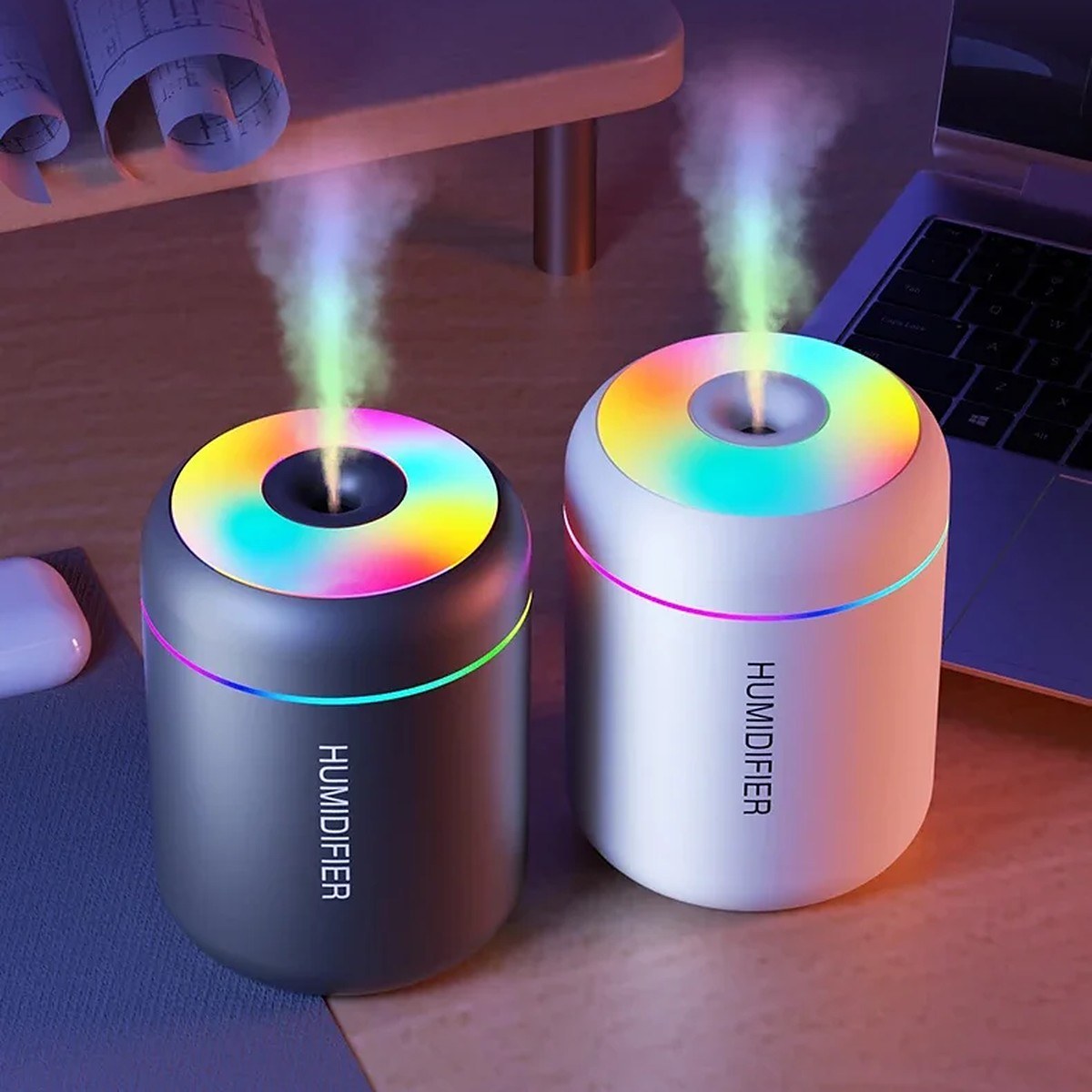 White and black Mini Glow Humidifiers misting on a desk at dusk with the color light on